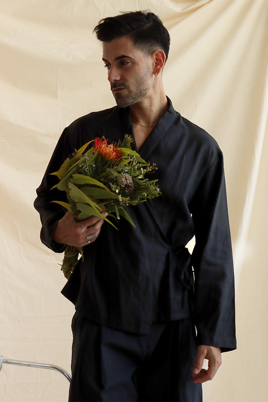 A man wearing a black wrap-tie-up linen shirt, with full sleeves and easy fit holding a bouquet of flowers.