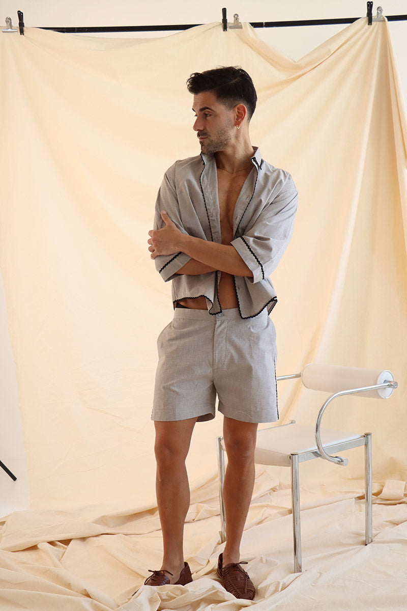 A person wearing a beige linen cropped shirt and matching shorts with wave trim, styled with a boxy silhouette and button-up front.