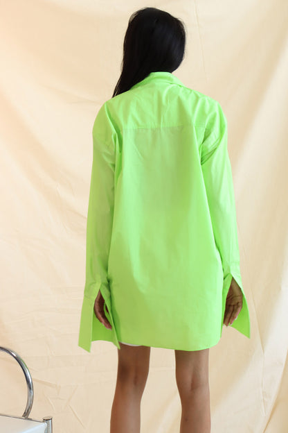 A person wearing a green button-down shirt with an oversized collar, styled in a knot, and full sleeves with oversized cuffs. The shirt has a curved, high-low hem.