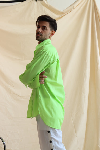 A person wearing a green button-down shirt with an oversized collar, styled in a knot, and full sleeves with oversized cuffs. The shirt has a curved, high-low hem.
