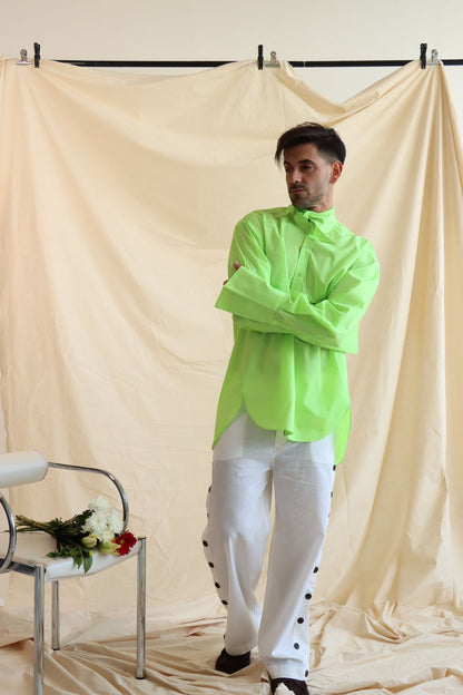 A person wearing a green button-down shirt with an oversized collar, styled in a knot, and full sleeves with oversized cuffs. The shirt has a curved, high-low hem.