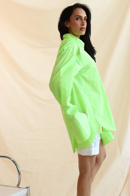 A person wearing a green button-down shirt with an oversized collar, styled in a knot, and full sleeves with oversized cuffs. The shirt has a curved, high-low hem.