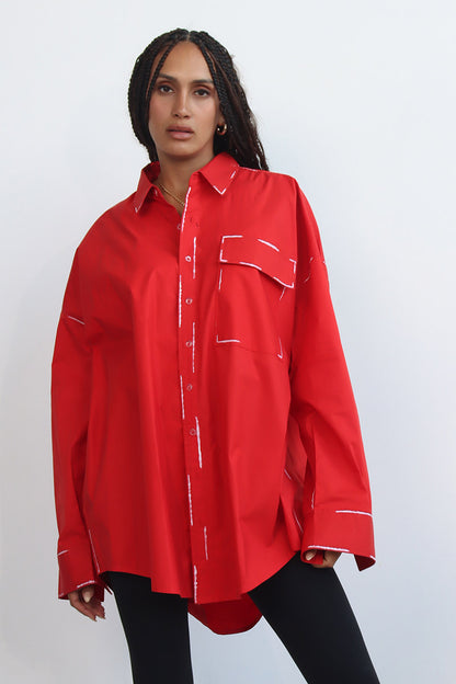 A person wearing a red long-sleeve shirt with a classic collar and black hand-painted details, paired with white pants.