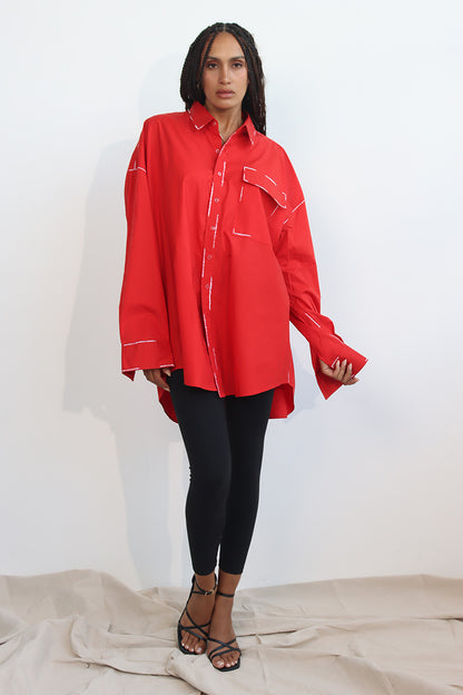 A person wearing a red long-sleeve shirt with a classic collar and black hand-painted details, paired with white pants.