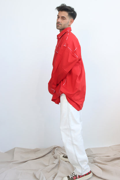 A person wearing a red long-sleeve shirt with a classic collar and black hand-painted details, paired with white pants.